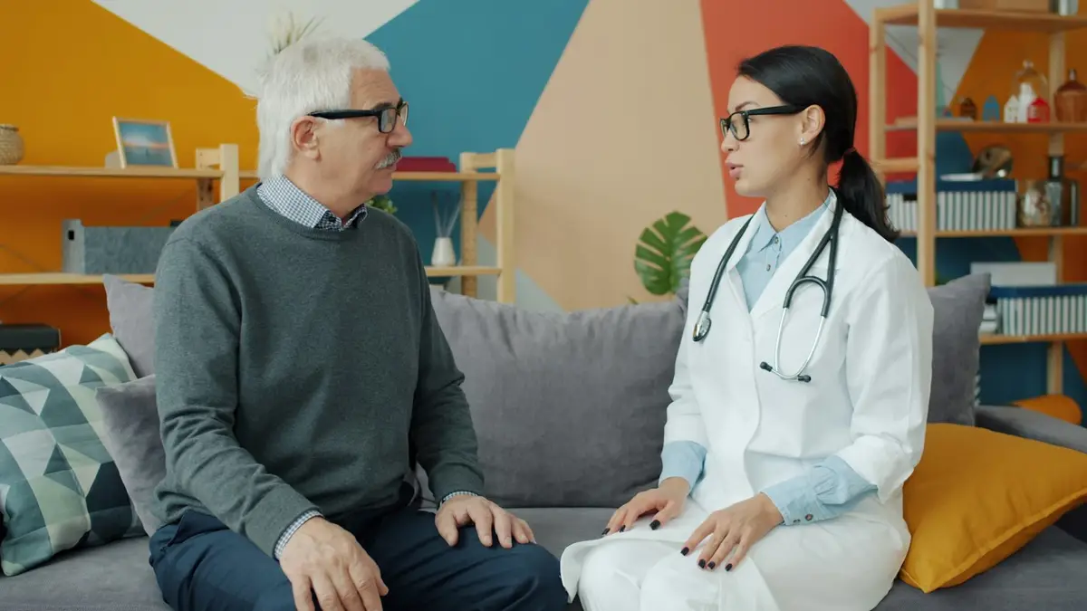 A doctor talking with an older patient on a sofa in a bright clinic
